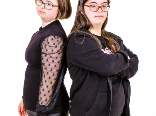 Two women standing back-to-back, both wearing black clothing and glasses.